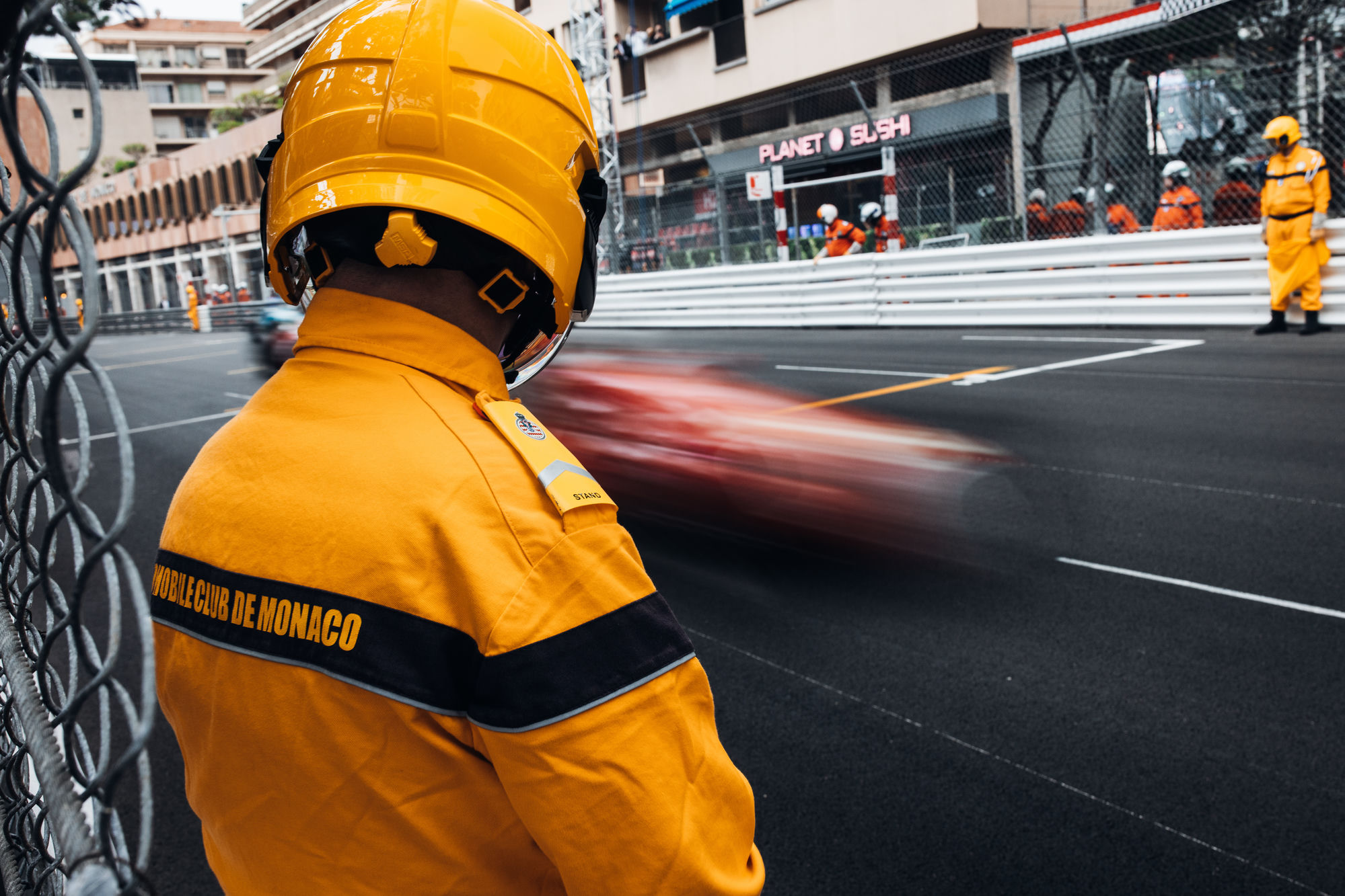 A trackside marshal in safety gear watching a race car pass